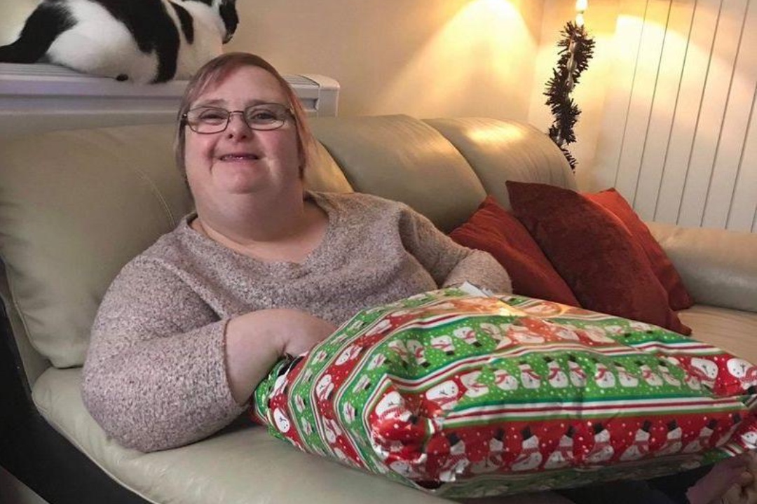 A woman smiling on a sofa holding a Christmas present in her supported living home